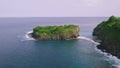 Drone view over the ocean with islet and cliffside covered with lush greenery.