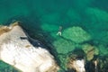 Drone view of a person diving in the sea surrounded by the rocks under the sunlight