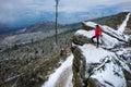 Drone view on a runner in a red sweatshirt stands on a rock and admires the mountain landscape.