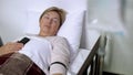 Drop counter close-up, mature female patient sleeping in sickbed with phone