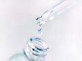 A drop falls from a pipette into a cosmetic bottle on a light background. Pipette with clear liquid. Facial skin care Royalty Free Stock Photo