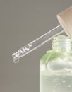 Drop falls from a pipette resting on a bottle filled with green serum agains gray, macro Royalty Free Stock Photo