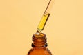 drop of liquid falling from a pipette into an amber bottle. Skincare products, natural cosmetic on orange background.