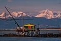 Drop net fishing hut at sunset against the Alps with snow, Marina di Pisa, Tuscany, Italy