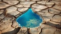 Drop shaped puddle of water in parched field with cracked soil. Drought, climate change, fresh water shortage and Royalty Free Stock Photo