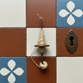 A drop spindle with beige yarn is positioned on decorative tiles. The tiles are square, Royalty Free Stock Photo