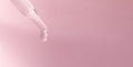 A dropping pipet, pipette, medicine dropper, dropping with transparent liquid or fluid, on pink background. Banner