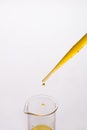 Dropping yellow liquid from a plastic pipette into a glass beaker