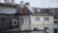 Drops going down on a window pane. Close-up of water droplets on glass. Rain with blur buildings in background. Cloudy day