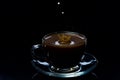 Drops of milk fall into a glass cup with black coffee, black background