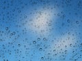 Drops of rain on glass with blue sky with white clouds defocused in background Royalty Free Stock Photo