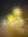 Drops of rain on window at night. Rainy and night city behind  glass. Tears of the sky flow down  transparent wall. Bead drops Royalty Free Stock Photo