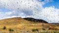 Drops of rain on the window on a rainy winter day in Los Angeles County, California; blurred hills covered by dry grass visible in Royalty Free Stock Photo