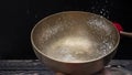 Drops of water fly into the air from hitting a Tibetan & x28;singing& x29; bowl. Cold boil. Tibetan bowl on a black