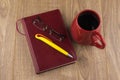 Drowsiness : diary, glasses, and a red mug of strong coffee on the wooden table, yellow ball-point pen on the book, the view from Royalty Free Stock Photo