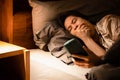 Drowsy woman lying in bed,addicted to her phone,constantly yawning,feeling tired,her heavy eyelids struggling to stay open,battled Royalty Free Stock Photo