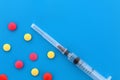 Loose pills and a syringe lie on a blue background.