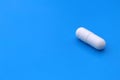 The drug in a white capsule lies alone on an isolated blue background. Royalty Free Stock Photo