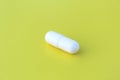 The drug in a white capsule lies alone on an isolated yellow background. Royalty Free Stock Photo