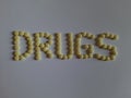 DRUGS, written by arrangement of yellow coated 100 mg Aspirin tablets on white paper background