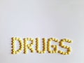 DRUGS, written by arrangement of yellow coated 100 mg Aspirin tablets on white paper background Royalty Free Stock Photo