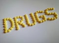 DRUGS, written by arrangement of yellow coated 100 mg Aspirin tablets on white paper background