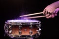 Drum sticks hitting snare drum with splashing water on black background under studio lighting