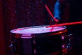 Drum sticks hitting snare drum with splashing water on dark background with red and blue studio lighting. Dynamic scene