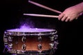 Drum sticks hitting snare drum with splashing water on black background under studio lighting