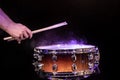 Drum sticks hitting snare drum with splashing water on black background under studio lighting