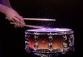 Drum sticks hitting snare drum with splashing water on black background under studio lighting