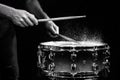 Drum sticks hitting snare drum with splashing water on black background under studio lighting. Black and white. Close up