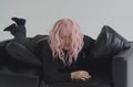 A drunk man in a pink wig is lying on the couch, waking up.