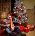 Drunk nerd in santa hat lying under the Christma tree with a lot