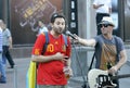 Drunk soccer Spanish fan wearing red T-shirt singing into the microphone on the street, the busker standing aside