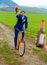 Drunken groom on a bike holding a wedding bouquet is running after a bride with a beer bottle.