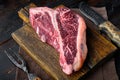 Dry-aged Raw T-bone or porterhouse beef marbled meat prime steak, on wooden cutting board, on old dark wooden table background