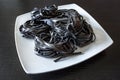 Dry black pasta with cuttlefish ink. Pasta of durum wheat semolina with squid ink on a square plate