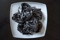Dry black pasta with cuttlefish ink. Pasta of durum wheat semolina with squid ink on a square plate