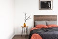 Dry branch in glass vase on wooden nightstand table nest to king size bed with orange and grey bedding