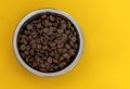 Dry brown pet food for cats or dogs in a metal bowl on a yellow background top view mock up, flat lay. Space for text Royalty Free Stock Photo