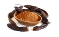 Dry carob powder in a wooden bowl and pods close up