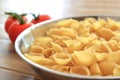 Dry conchiglie pasta shells in a stainless steel bowl with vine tomatoes in the blurred background Royalty Free Stock Photo