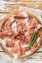 Dry cured parma ham or Prosciutto crudo on a wooden board with rosemary. White wooden background. Top View