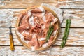 Dry cured parma ham or Prosciutto crudo on a wooden board with rosemary. White wooden background. Top View