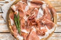 Dry cured parma ham or Prosciutto crudo on a wooden board with rosemary. White wooden background. Top View