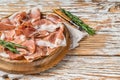 Dry cured parma ham or Prosciutto crudo on a wooden board with rosemary. White wooden background. Top View. Copy space