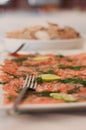 Dry-cured salmon, gravlax or gravlaks with lime slices, dill and pepper on a white dish with a fork. Other appetizers in the