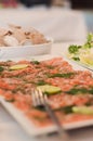 Dry-cured salmon, gravlax or gravlaks with lime slices, dill and pepper on a white dish with a fork. Other appetizers in the