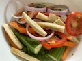 Dry cut vegetables like raw plantain onion rings tomatoes carrots and moringa placed on a white bowl